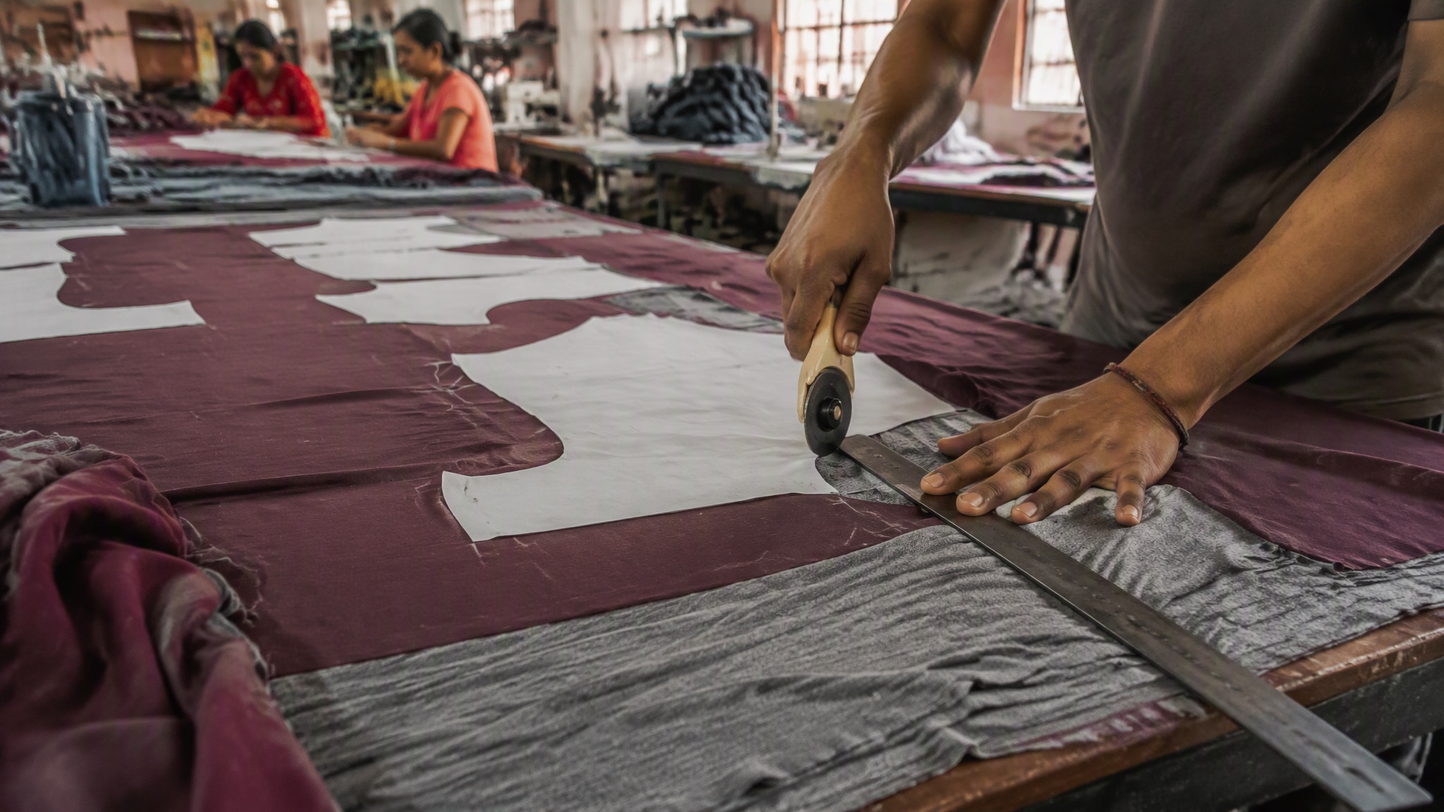 A cutter guiding a rotary blade along chalk lines through layered plum fabric at the Hamsa Wears factory
